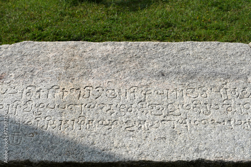 Inscriptions of Tamil language carved on the stone with green grass in the background. Indian rock art relief carvings of Historical ancient vintage Tamil text in Temples. 