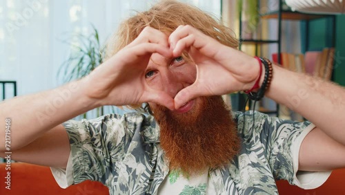 I love you. Happy Caucasian man at home living room couch makes symbol of love, showing heart sign to camera, express romantic feelings express sincere positive feelings. Charity, gratitude, donation