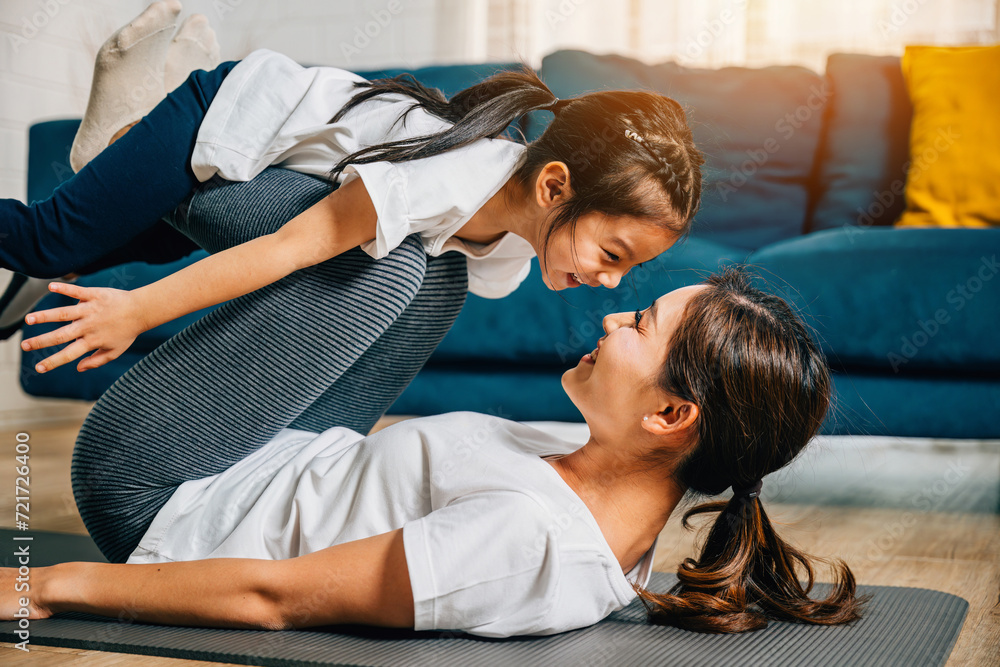 A mother holds her child in a playful family fitness pose imagining themselves 'flying' like airplanes during their Pilates and yoga routine promoting trust harmony and happiness. A mother holds her child in a playful family fitness pose imagining themselves 'flying' like airplanes during their Pilates and yoga routine promoting trust harmony and happiness.