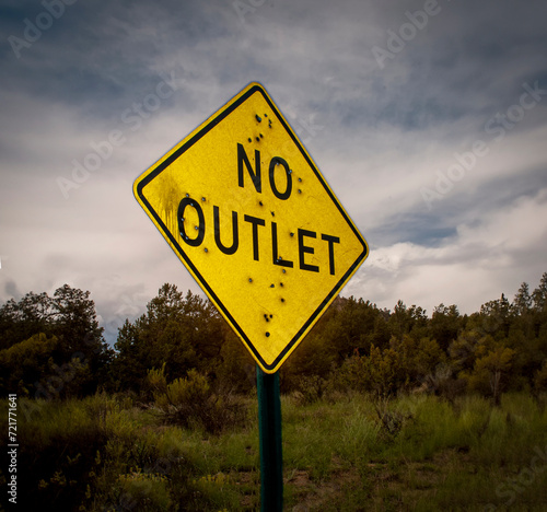 A road sign stating No Outlet riddled with bullet holes