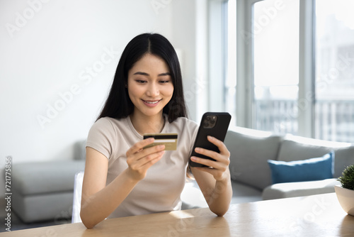 Positive young Asian woman paying by credit card on ecommerce service, using online bank application on smartphone for business financial communication, shopping on Internet, booking hotel