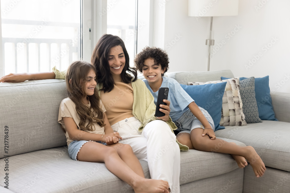 Happy mom and two sibling kids using application on mobile phone for online communication, relaxing together on couch, looking at screen, smiling, laughing, having fun, talking on video call Happy mom and two sibling kids using application on mobile phone for online communication, relaxing together on couch, looking at screen, smiling, laughing, having fun, talking on video call