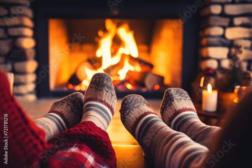 Feet in woollen socks by the Christmas fireplace. Couple sitting under the blanket, relaxes by warm fire and warming up their feet in woollen socks. Winter and Christmas holidays concept. photo
