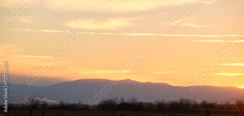 Fototapeta Naklejka Na Ścianę i Meble -  Beautiful evening panoramic landscape with bright setting sun over distant mountain peaks at sunset