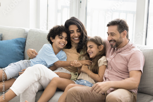 Cheerful parents embracing tickling little kids on home couch  enjoying active games  leisure  family activities with children  laughing  having fun with giggling son and daughter