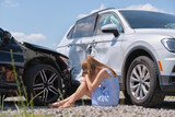 Sad female driver sitting on street side shocked after car accident. Road safety and vehicle insurance concept