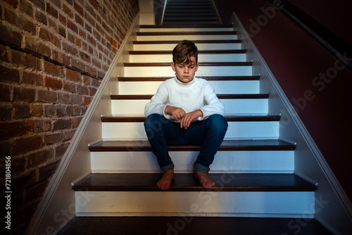 Sad and lonely barefoot boy in white sweater sitting alone on a staircase © 3Days2Go Media