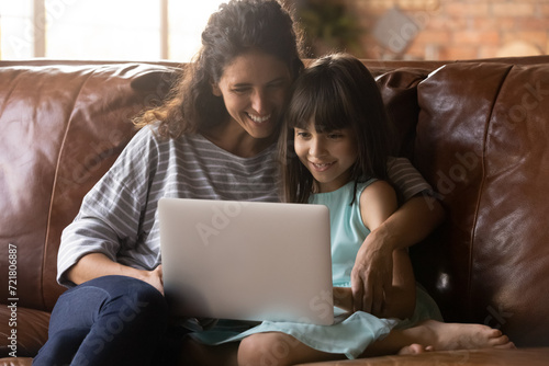 Parental control. Smiling latina mommy and preteen junior school age daughter child chat in computer app make purchases at web shop online. Happy young nanny and little girl friends use laptop at home