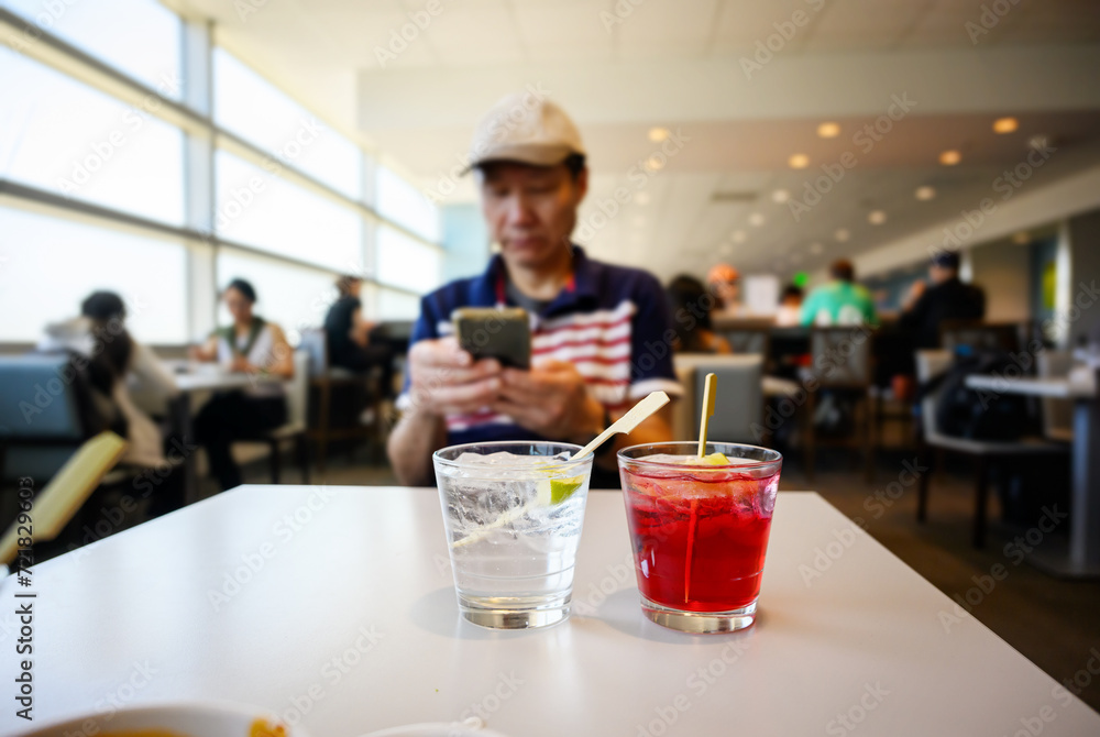 People enjoying snacks and drinks at the airport lounge. Man checking his smartphone, cocktail drinks on the table.