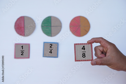 Hand hold paper card with fraction numbers. Circle paper show parts of color separation. Concept, Math teaching. Education. DIY craft as teaching aid in Math subject.            