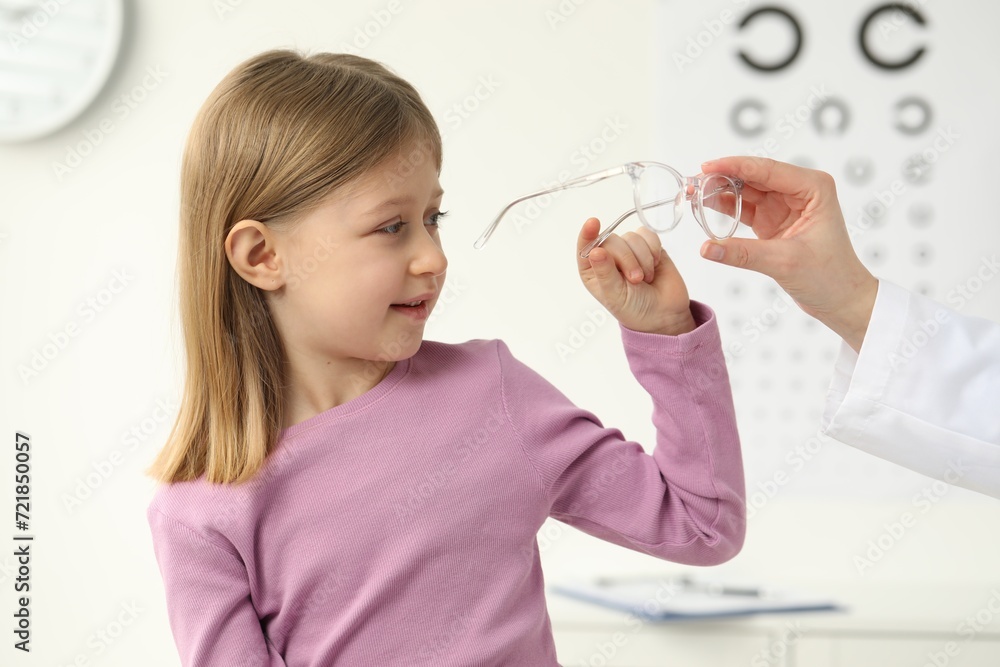 Vision testing. Ophthalmologist giving glasses to little girl indoors Vision testing. Ophthalmologist giving glasses to little girl indoors