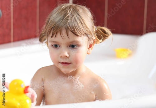 Little girl bathing with toy duck in tub at home, selective focus