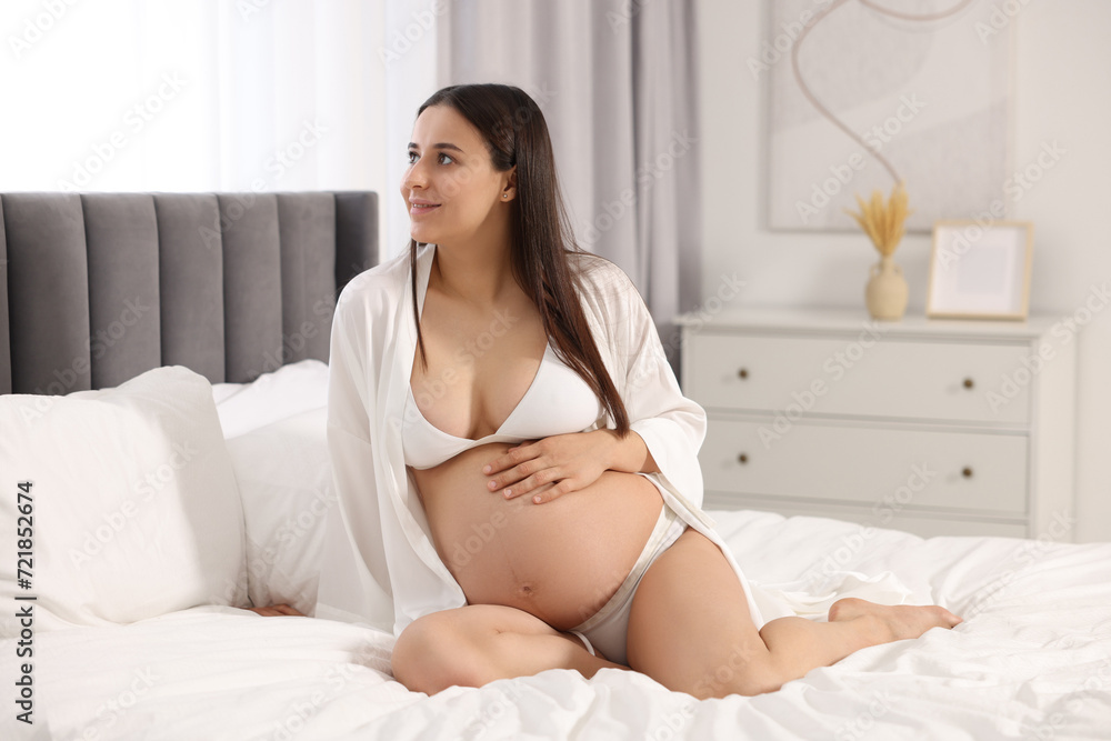 Beautiful pregnant woman in stylish comfortable underwear and robe on bed at home Beautiful pregnant woman in stylish comfortable underwear and robe on bed at home