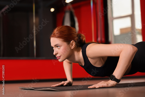 Athletic young woman doing push ups on mat in gym, space for text