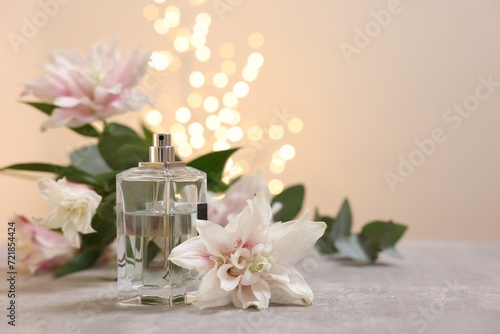 Bottle of perfume and beautiful lily flowers on table against beige background with blurred lights  space for text