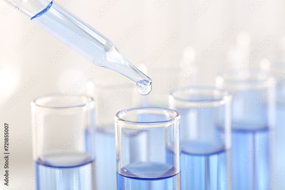 Laboratory analysis. Dripping light blue liquid from pipette into glass test tube on blurred background, closeup Laboratory analysis. Dripping light blue liquid from pipette into glass test tube on blurred background, closeup