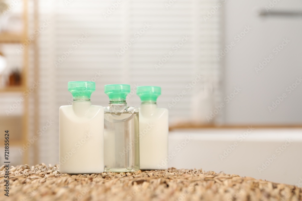 Mini bottles of cosmetic products on wicker mat against blurred background. Space for text Mini bottles of cosmetic products on wicker mat against blurred background. Space for text