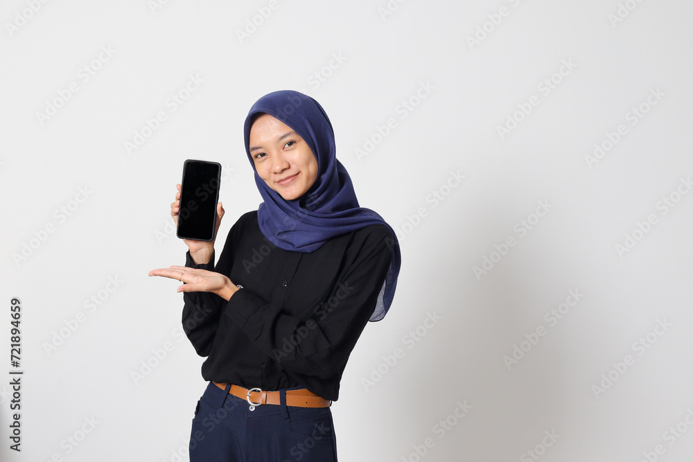 Portrait of excited Asian hijab woman in casual shirt showing blank screen mobile phone mockup while pointing and presenting product. Isolated image on white background Portrait of excited Asian hijab woman in casual shirt showing blank screen mobile phone mockup while pointing and presenting product. Isolated image on white background