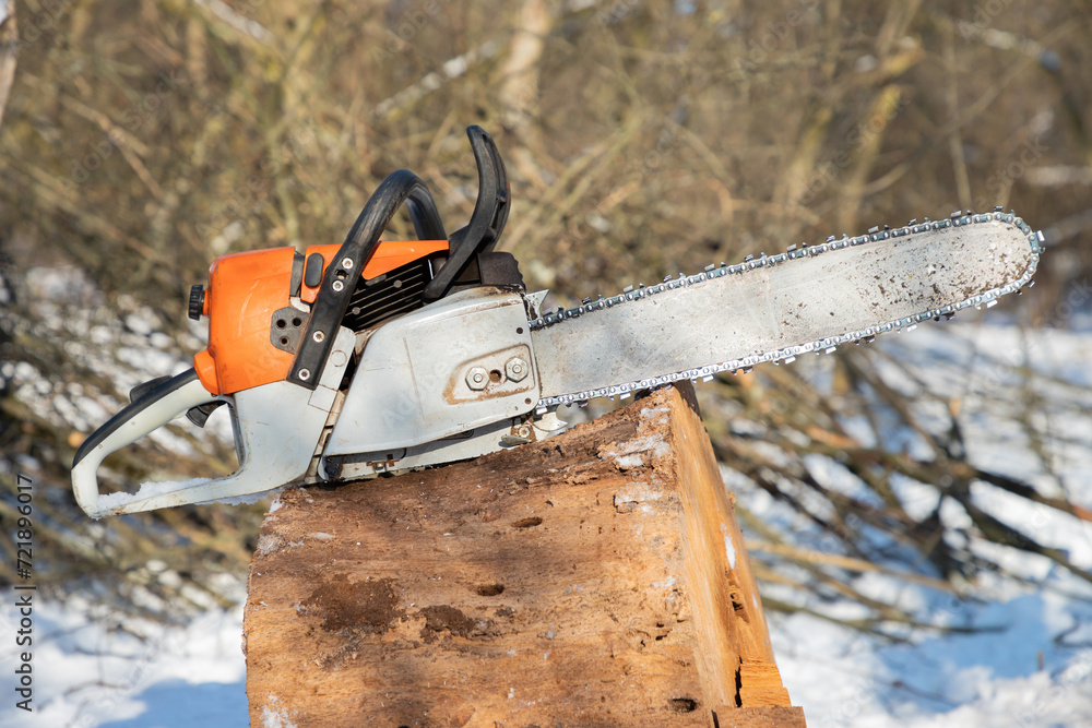 Petrol or electric battery powered chainsaw. Chainsaw on wooden stump or firewood. Firewood processing.