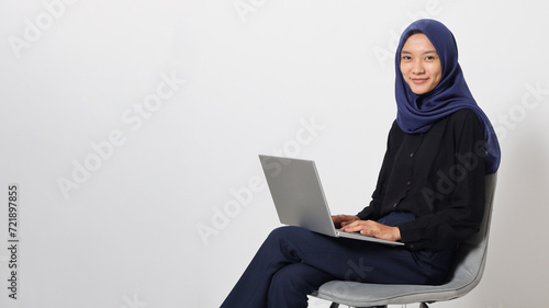 Portrait of excited Asian hijab woman in casual shirt sitting on chair, working on laptop. An employee or student doing her task and job . Businesswoman concept. Isolated image on white background photo