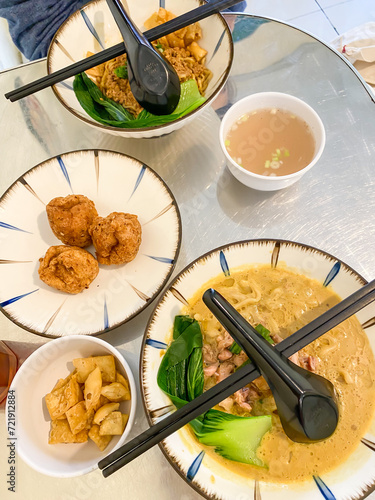 Eating chinese noodle soup topped with dumplings, chicken or beef meat, meatballs, vegetables served in ceramic bowls on a wooden table. photo