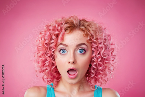 Portrait of attractive amazed girl with pink curly hair on pink background