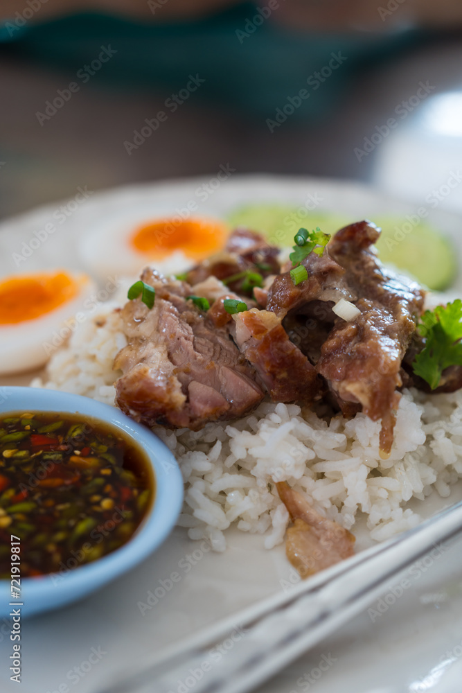 Slice of braised pork placed on hot steamed rice served with boiled egg and sliced cucumber