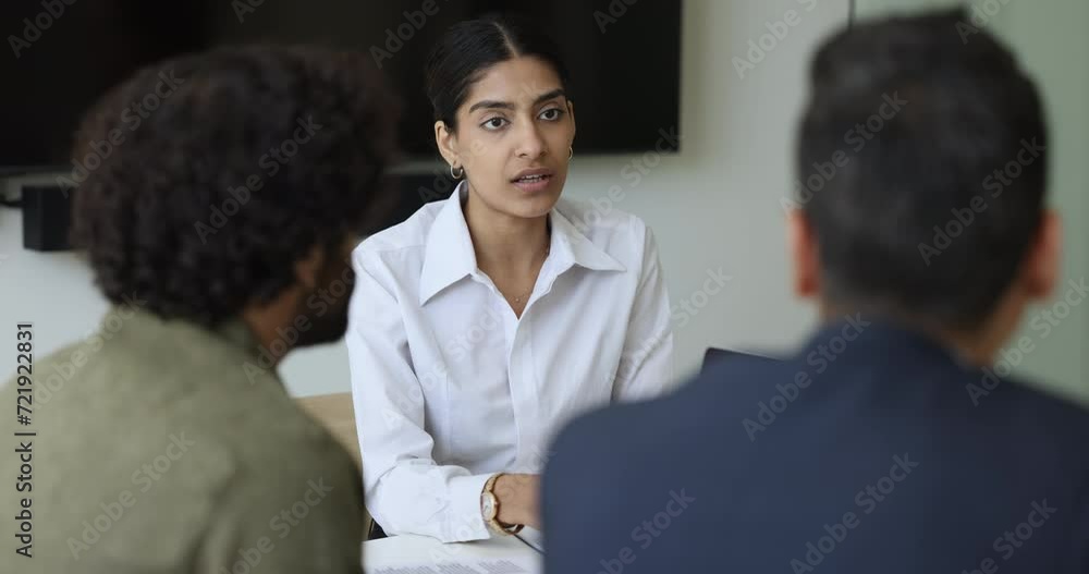 Confident young Indian businesswoman talking to diverse male colleagues at meeting table, getting cheerful, laughing. Multiethnic business team cooperating on project, brainstorming Confident young Indian businesswoman talking to diverse male colleagues at meeting table, getting cheerful, laughing. Multiethnic business team cooperating on project, brainstorming