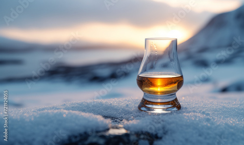 Single malt whisky in a tulip glass set upon snowy terrain with a soft glow of the sunset in a winter landscape. Design for exclusive spirit labels and winter travel experiences