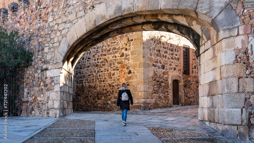Tourist woman passing through the entrance arch in the wall that gives access to Caceres, Spain.