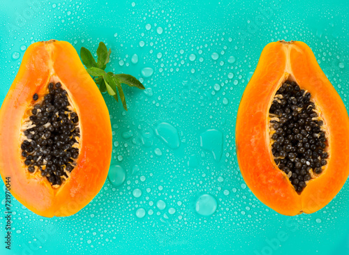 Papaya fruit on blue background with water drops, fresh exotic fruits border design. Half of fresh organic Papayas exotic fruit with leaf close up. Top view 
