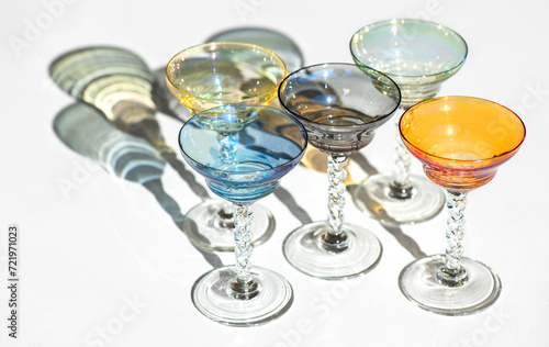 Crystal colorful stemware set with reflection over white background. Colourful elite set of empty alcohol liquor glasses on white, border design. Stemmed glasses, drinkware
