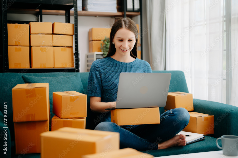 Young business owner woman prepare parcel box and standing check online orders for deliver to customer on tablet, laptop Shopping Online concept. on sofa .. Young business owner woman prepare parcel box and standing check online orders for deliver to customer on tablet, laptop Shopping Online concept. on sofa ..