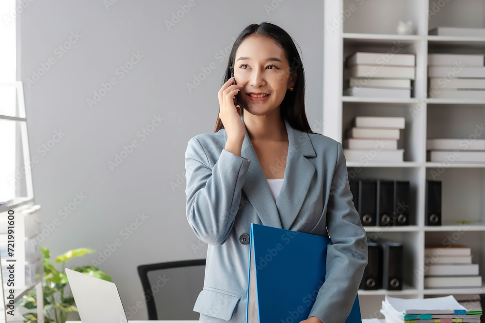 Beautiful female employee using the phone in the office, Young happy businesswoman using computer in office, portrait of a young businesswoman working on a laptop in an office Beautiful female employee using the phone in the office, Young happy businesswoman using computer in office, portrait of a young businesswoman working on a laptop in an office