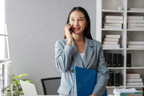 Beautiful female employee using the phone in the office, Young happy businesswoman using computer in office, portrait of a young businesswoman working on a laptop in an office