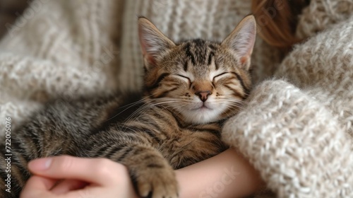 A cute tabby kitten sleeping in a woman's arms