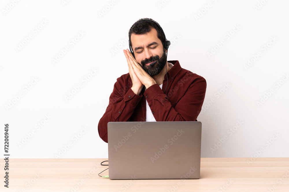 Telemarketer caucasian man working with a headset and with laptop making sleep gesture in dorable expression. Telemarketer caucasian man working with a headset and with laptop making sleep gesture in dorable expression.