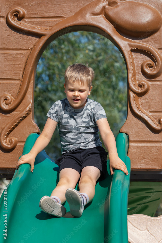 A happy little boy sliding down a plastic green slide through a brown octopus figure arch A happy little boy sliding down a plastic green slide through a brown octopus figure arch