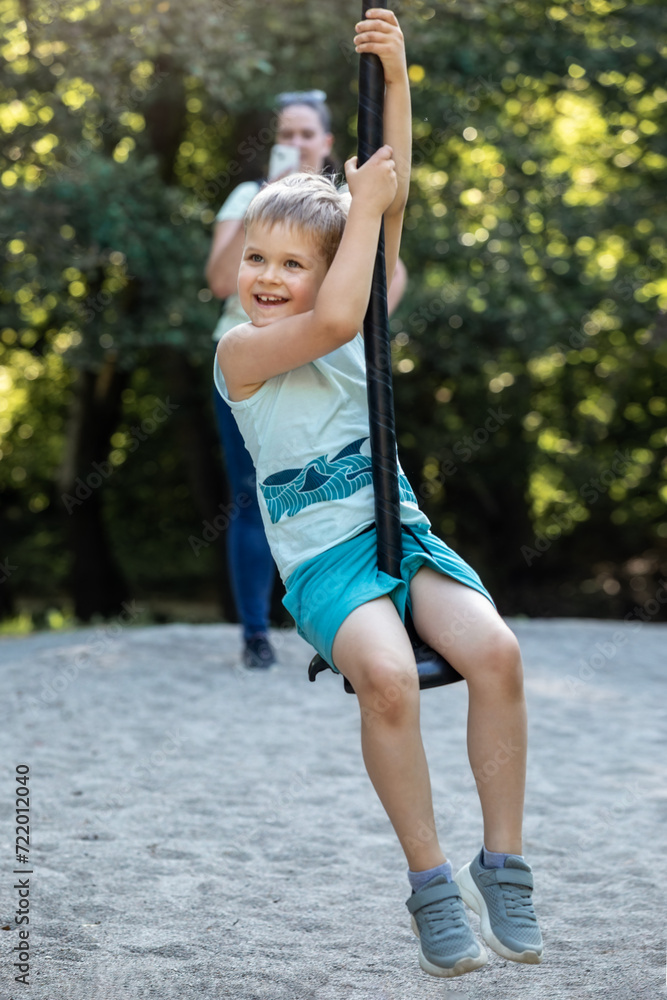 With a very satisfied smile, the child rides down the rope swing while his mother takes a picture of him from behind With a very satisfied smile, the child rides down the rope swing while his mother takes a picture of him from behind