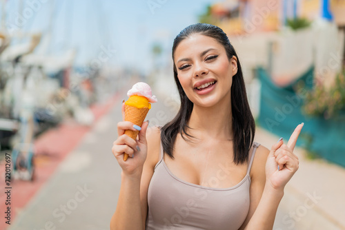 Young pretty woman with a cornet ice cream at outdoors pointing up a great idea