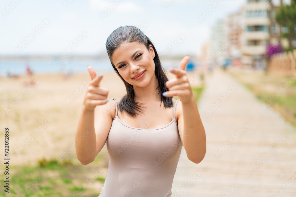 Young pretty woman at outdoors points finger at you while smiling