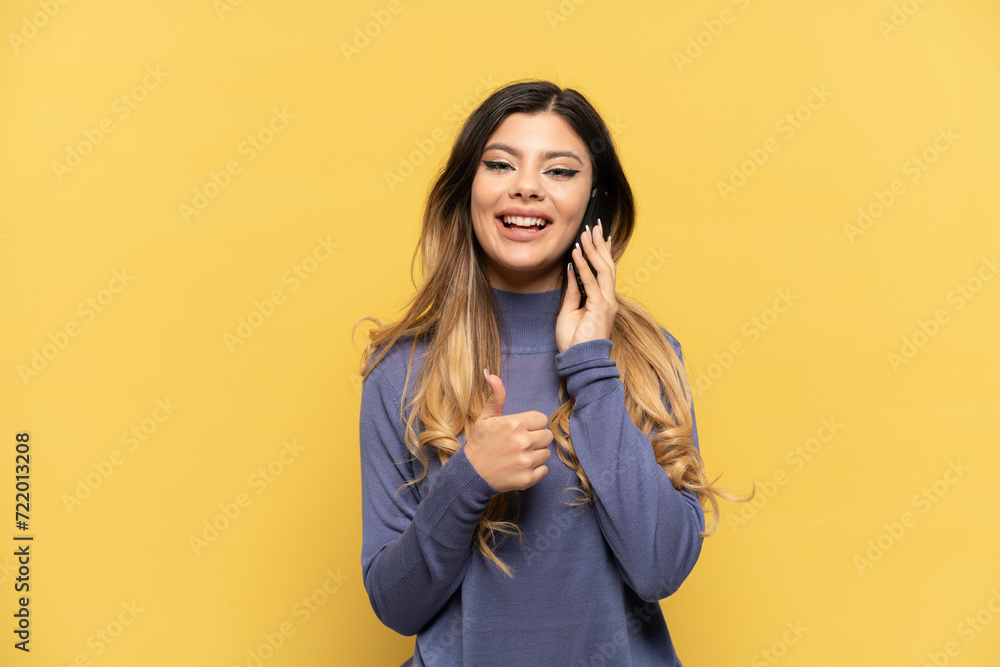 Young Russian girl using mobile phone isolated on yellow background giving a thumbs up gesture Young Russian girl using mobile phone isolated on yellow background giving a thumbs up gesture