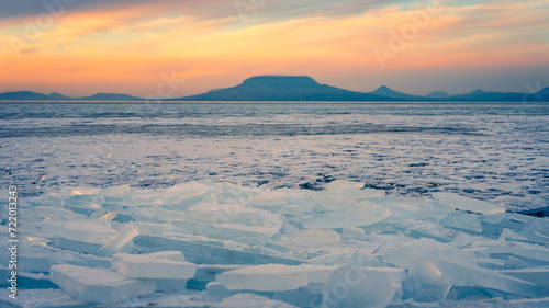 onyod, Hungary - Beautiful icebergs on the shore of the frozen Balaton. Badacsony and Gulacs with a spectacular cloudy sunset in the background. Winter landscape. photo