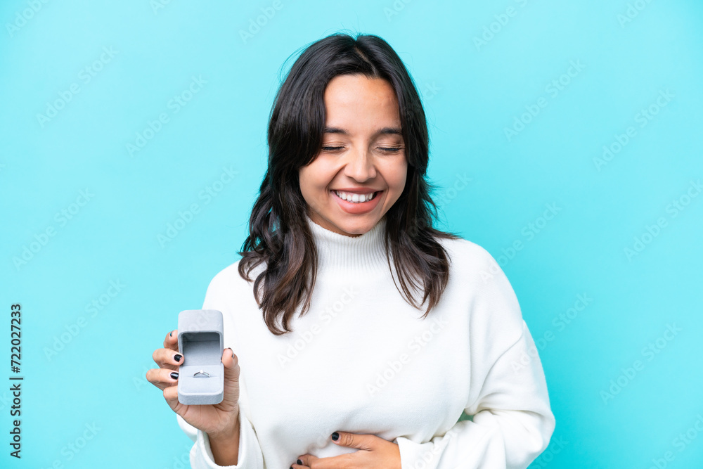Young hispanic woman holding a engagement ring isolated on blue background smiling a lot Young hispanic woman holding a engagement ring isolated on blue background smiling a lot