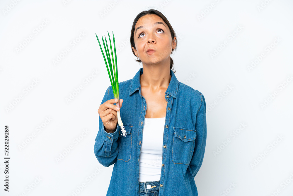 Young hispanic woman holding chive isolated on white background and looking up Young hispanic woman holding chive isolated on white background and looking up