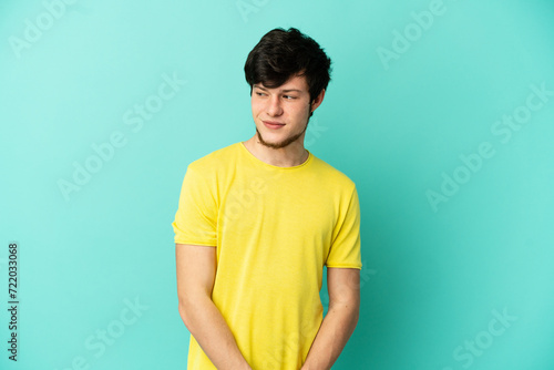Young Russian man isolated on blue background having doubts while looking side