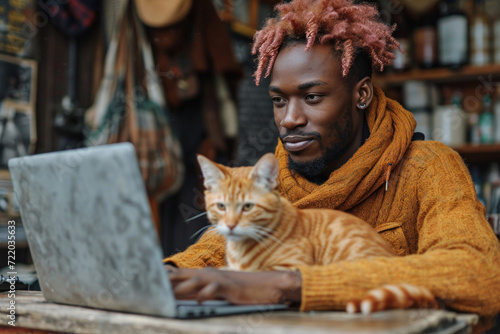 Young man working on a laptop at home, accompanied by his cute grey cat, blending business with the comfort of domestic life.