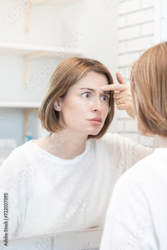 Young beautiful woman looking at mirror and confusing because of new wrinkles	