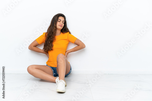 Young caucasian woman sitting on the floor isolated on white background suffering from backache for having made an effort