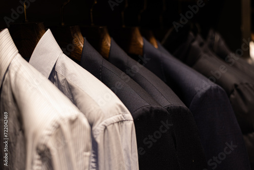 wardrobe with men's clothes in dark colors. jacket, down jacket, shirt. The clothes are neatly hung on wooden hangers
